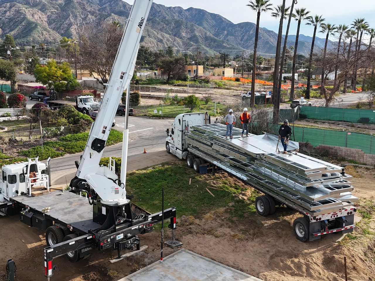 Panelized light gauge steel wall and floor panels arriving by flatbed with crane and crew at a jobsite