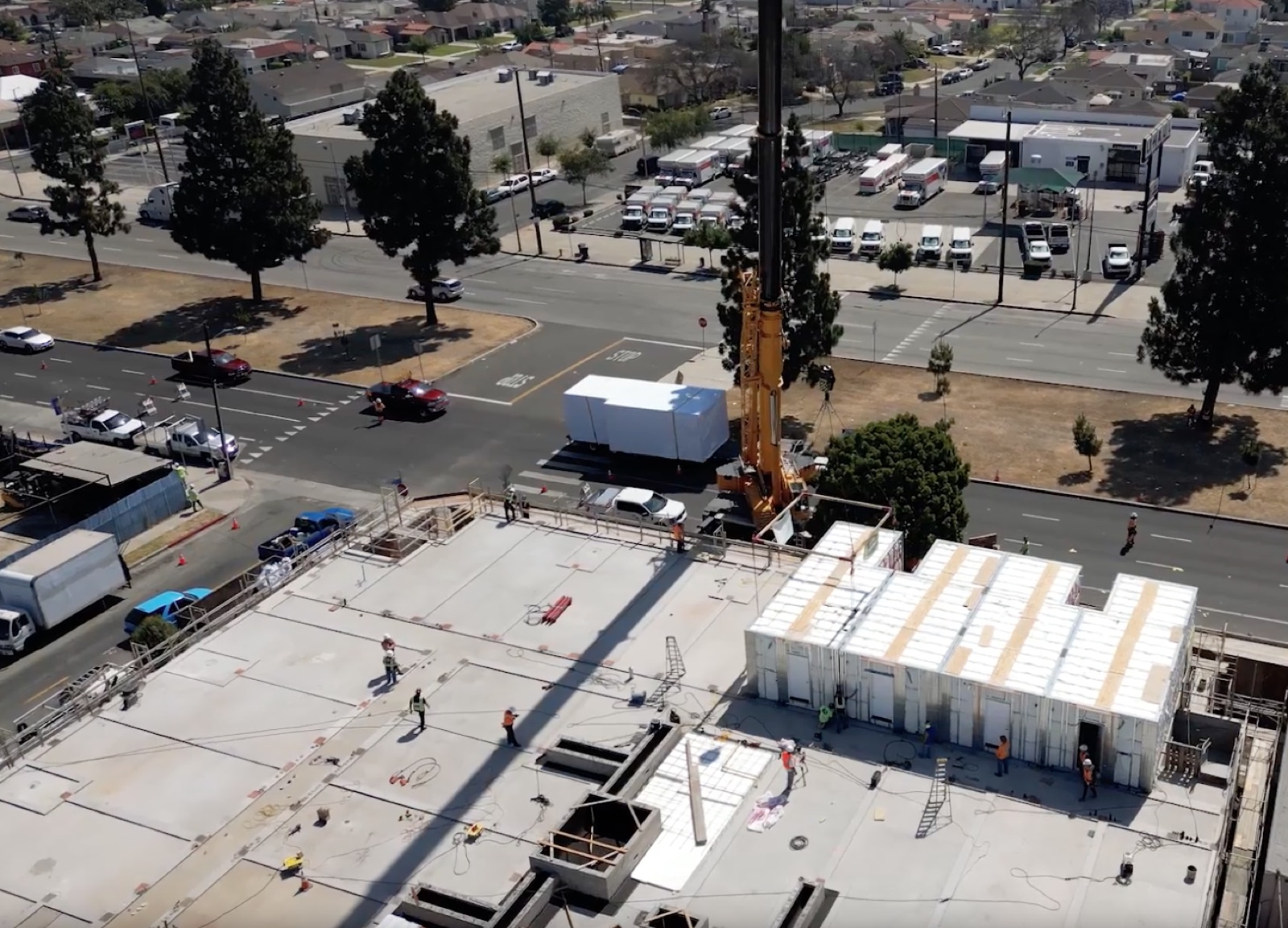 A tower crane lowering a wrapped volumetric module onto the prepared concrete podium deck